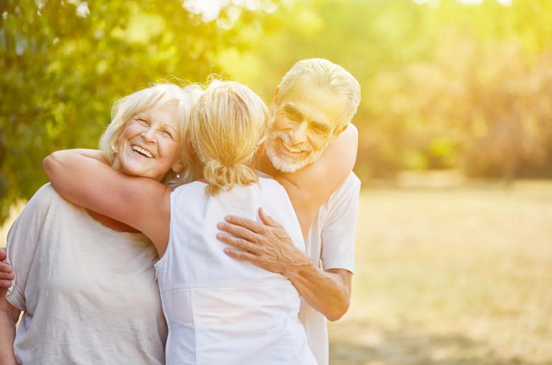 Senior couple hugging their insurance agent outdoors, smiling with peace of mind