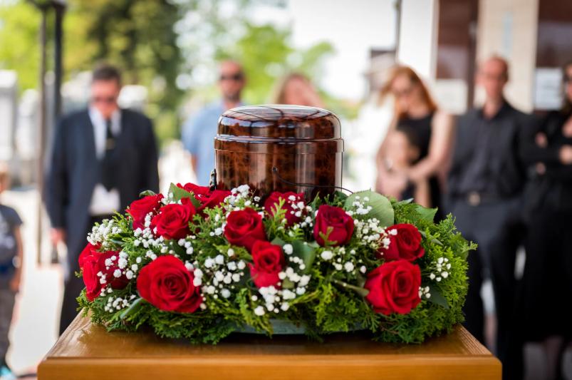 Funeral urn with red roses and family members mourning in background