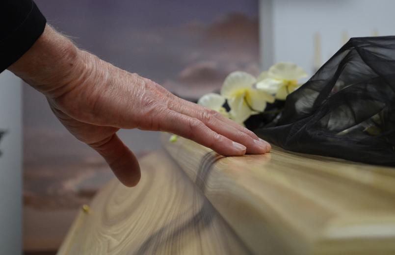 Elderly hand resting on a wooden casket during a funeral