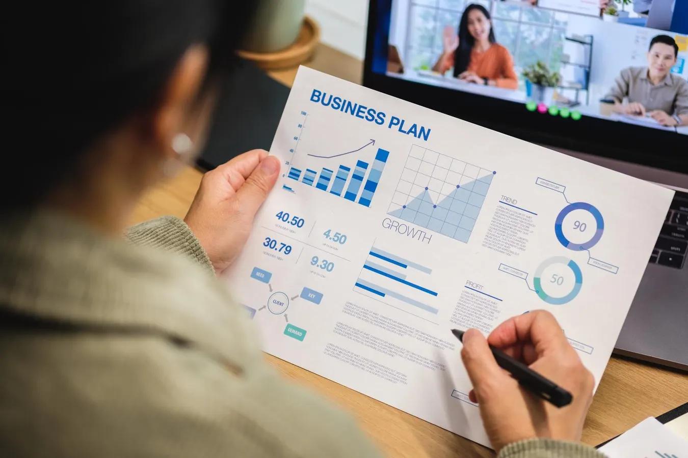 Insurance agent holding a business plan with graphs and charts during a video meeting