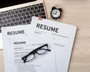 Stack of resumes with eyeglasses and laptop, ready for job application