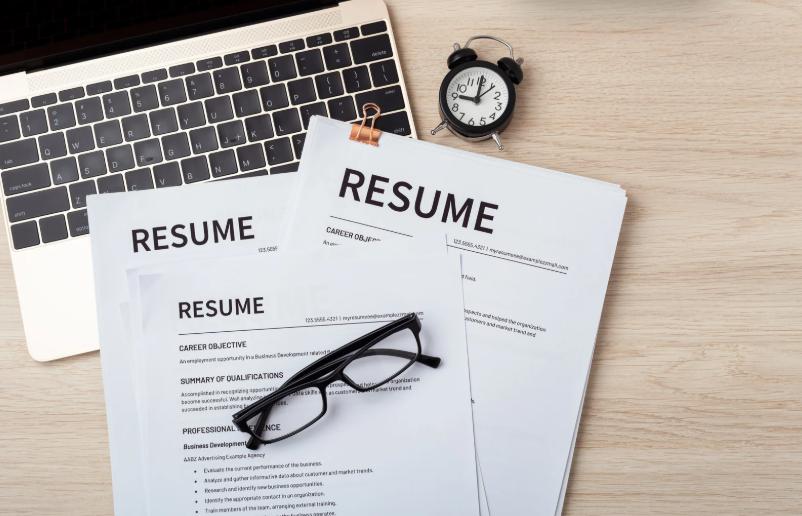 Stack of resumes with eyeglasses and laptop, ready for job application