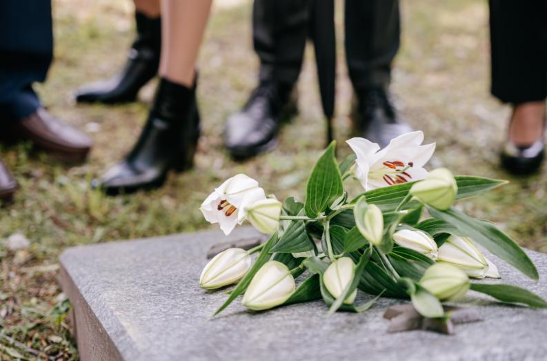 Funeral flowers on gravestone with people standing in background