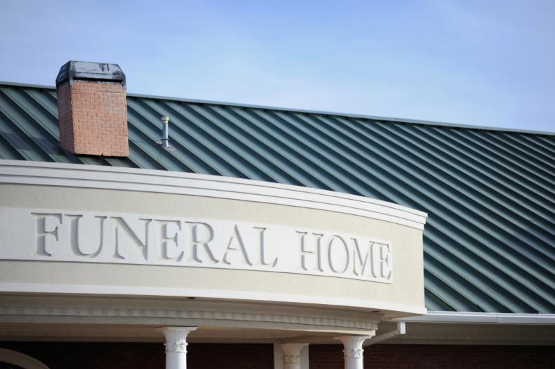 Funeral home building exterior with green metal roof and white stone sign