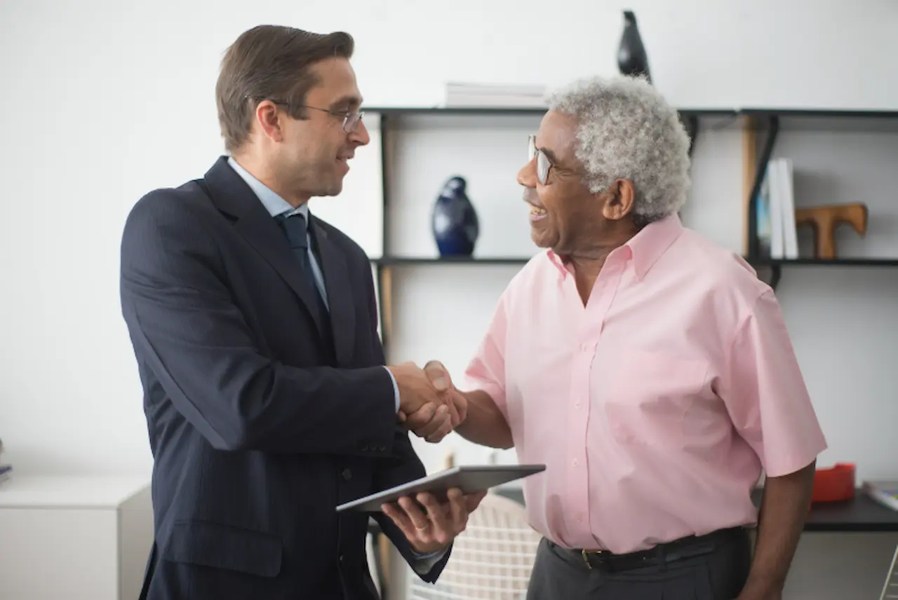 Life insurance agent shaking hands with a senior client in an office