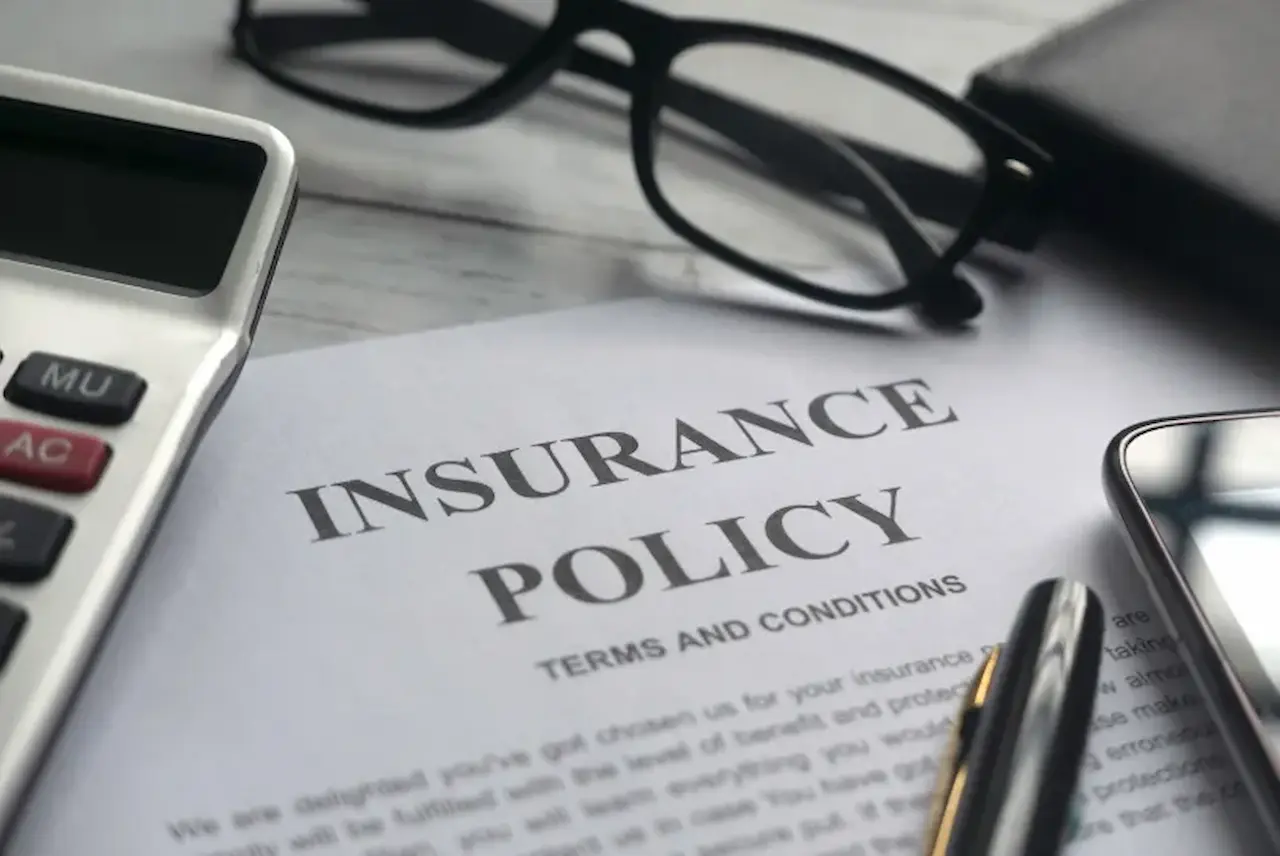 Insurance policy document with pen, calculator, and glasses
