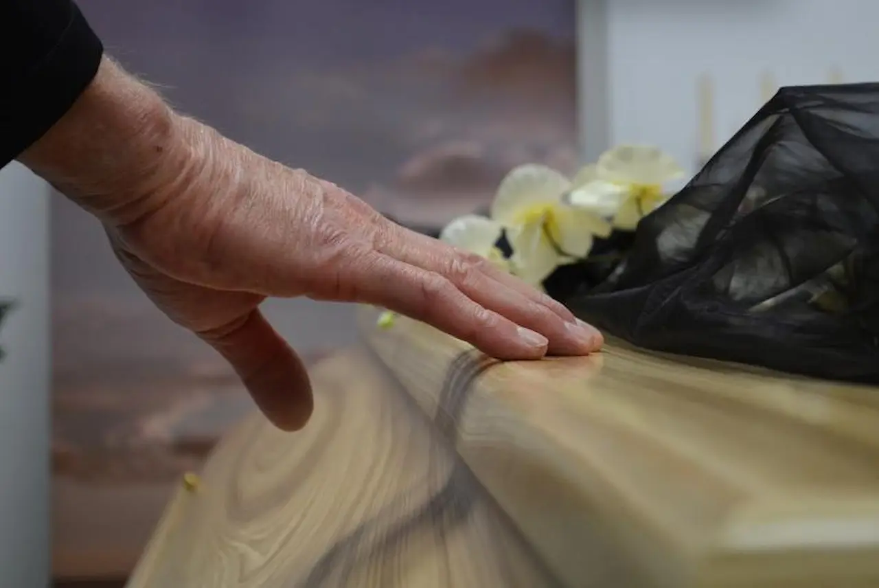 Final Farewell with Funeral Coverage Elderly hand resting on a wooden casket during a funeral