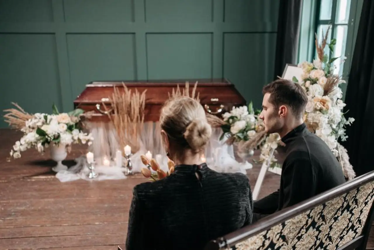 Man and woman sitting near decorated wooden casket during funeral service